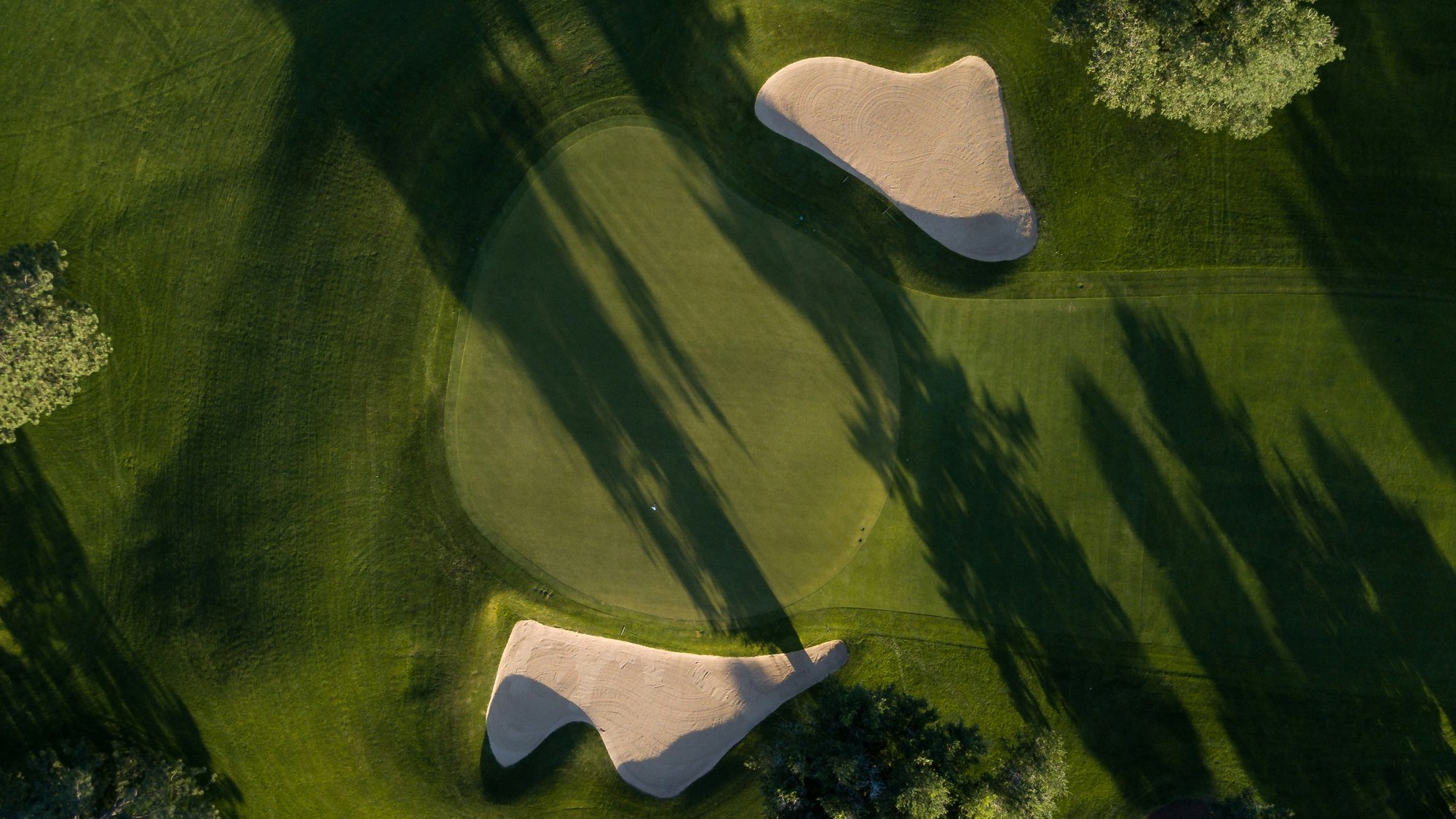 Aerial view of a green with two bunkers and long afternoon shadows