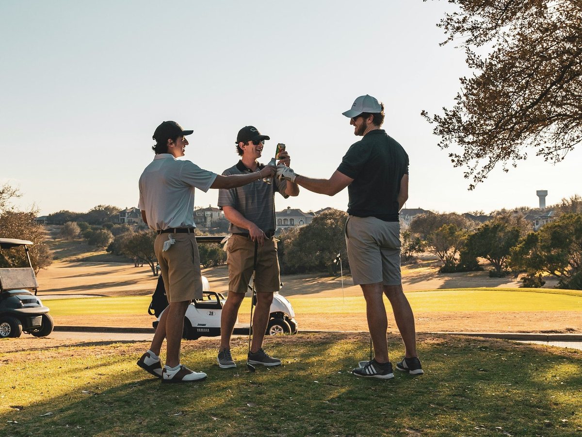Three golfers toasting beside a cart at the end of a round