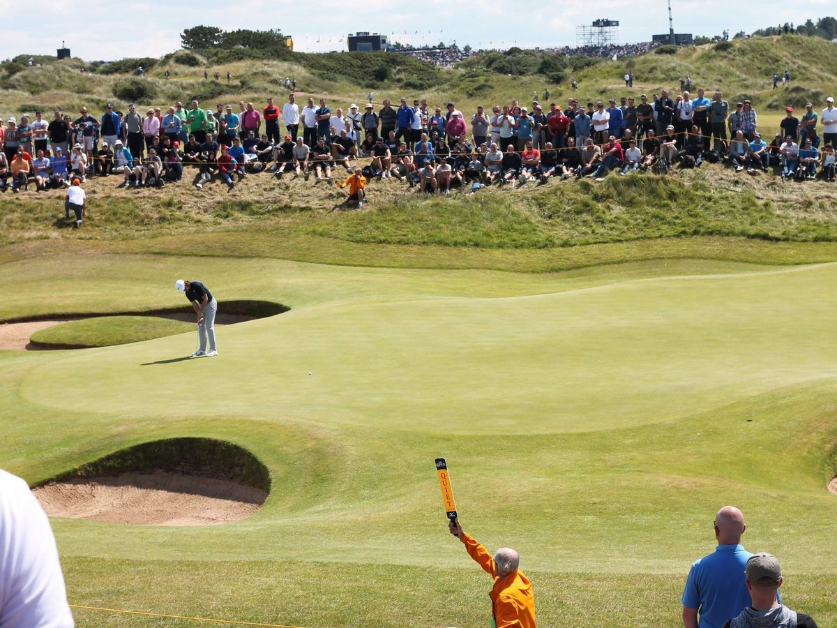 Spectators around a links green and bunkers