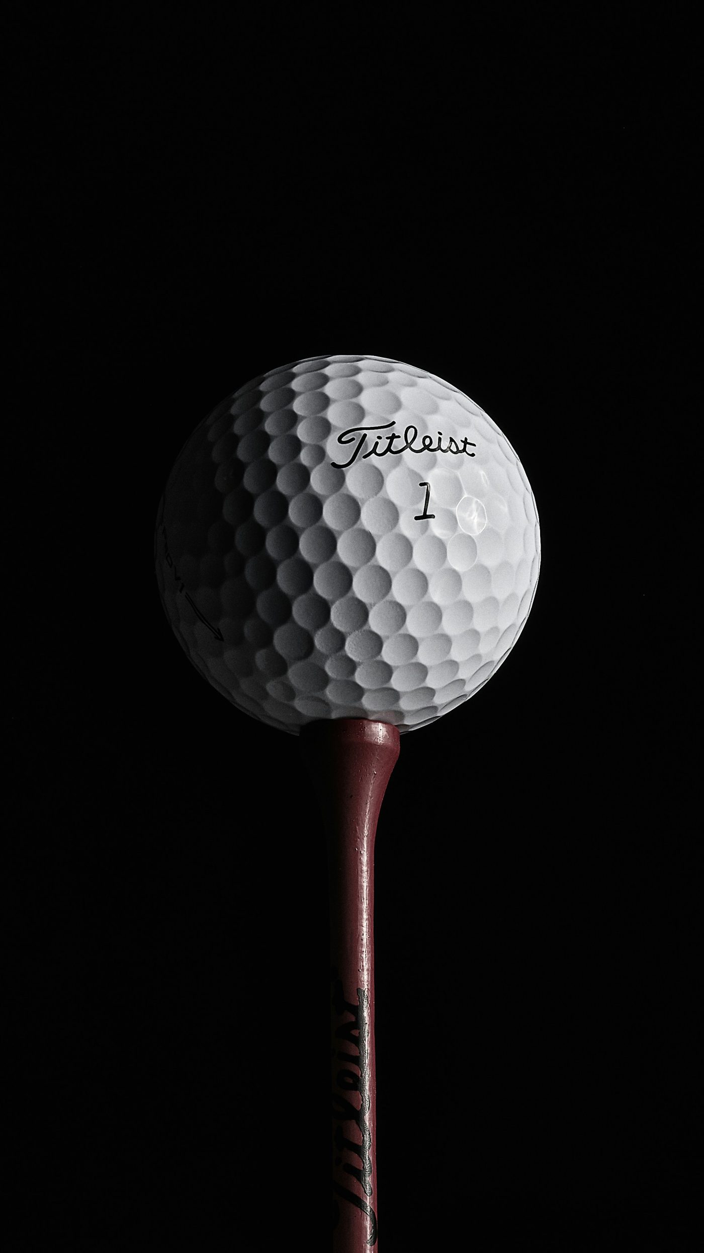 A white Titleist golf ball on a tee against a black background